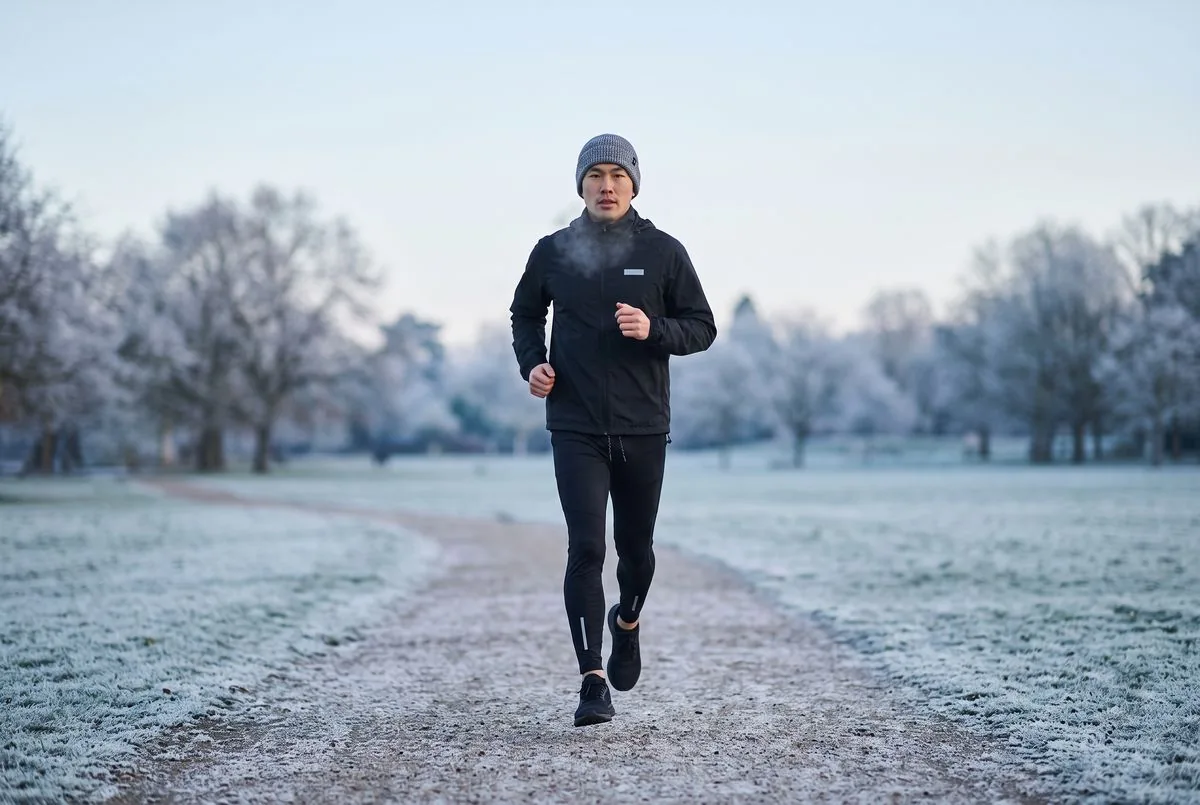 Běžec v černé bundě Kinetra Wind, černých legínách Kinetra Run a šedé čepici Horvik na ojíněné cestě v parku