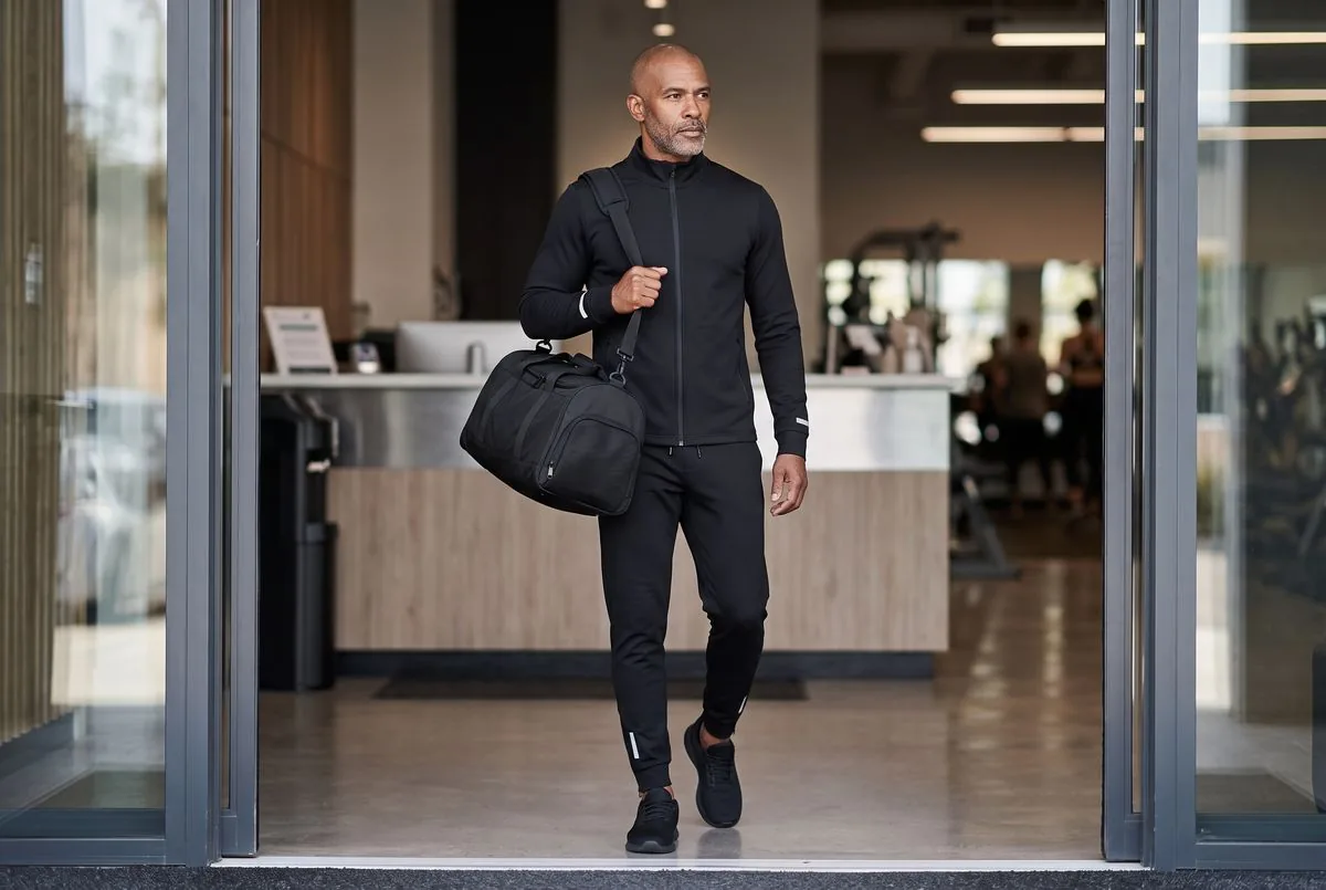 Muž v černé soupravě Kinetra Tech přichází s taškou Kinetra Duffel do posilovny